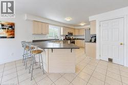 Kitchen featuring light wood-finish cabinetry, solid surface countertops, stainless steel appliances, and tiled flooring - 