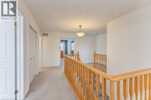 Carpeted hallway with wood banister, white paneled doors, and a semi-flush mount ceiling light fixture - 88 Decaro Crescent, Cambridge, ON 