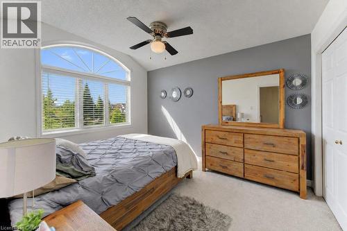 Arched window with louvered blinds, vaulted ceiling, ceiling fan with integrated lighting, wood-finish dresser with integrated mirror, and plush carpet flooring - 88 Decaro Crescent, Cambridge, ON 