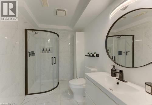 Curved glass shower enclosure with matte black framing, white tile walls and flooring, white vanity with integrated sink, matte black faucet, and a large round mirror - 88 Decaro Crescent, Cambridge, ON 