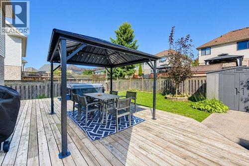 Expansive wood-finish deck with a black metal gazebo, integrated hot tub, manicured lawn, and a grey utility shed - 88 Decaro Crescent, Cambridge, ON 