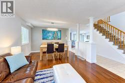 Living area featuring wood-finish flooring, dining area with modern chandelier, and staircase with wood railing - 