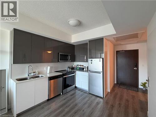 Modern kitchen featuring sleek gray upper cabinetry, white lower cabinetry, stainless steel appliances, wood-finish flooring, and a white backsplash - 60 Frederick Street Unit# 1213, Kitchener, ON 