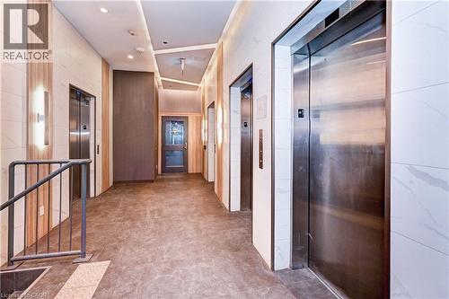 Elevator lobby featuring multiple stainless steel elevator doors, recessed ceiling lighting, wall-mounted sconces, and wood-finish wall panels - 60 Frederick Street Unit# 1213, Kitchener, ON 
