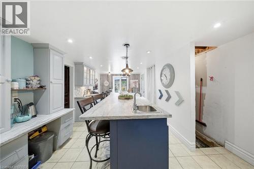 Spacious kitchen featuring a large island with an integrated sink, pendant lighting, built-in cabinetry, tiled flooring, and recessed ceiling lights - 62 East Avenue, Brantford, ON 