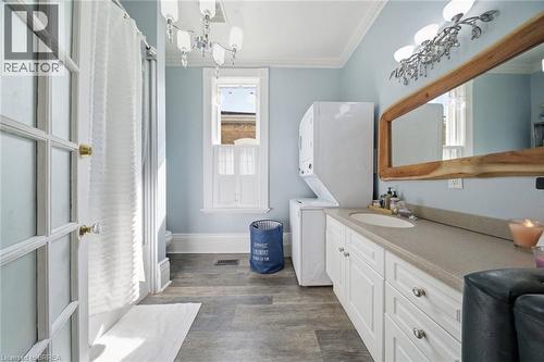 Full bathroom featuring a single-sink vanity with ample countertop space, wood-finish flooring, a stacked washer and dryer, and a window with white trim - 62 East Avenue, Brantford, ON 