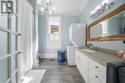 Full bathroom featuring a single-sink vanity with ample countertop space, wood-finish flooring, a stacked washer and dryer, and a window with white trim - 