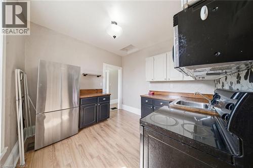 Galley kitchen featuring wood-finish flooring, two-tone cabinetry with black base cabinets and white upper cabinets, wood countertops, and a black and white floral patterned backsplash - 62 East Avenue, Brantford, ON 