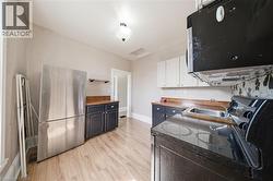 Galley kitchen featuring wood-finish flooring, two-tone cabinetry with black base cabinets and white upper cabinets, wood countertops, and a black and white floral patterned backsplash - 