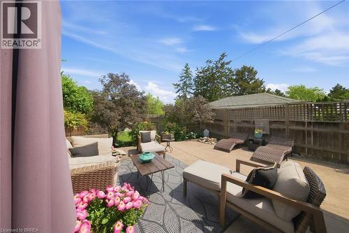 Spacious concrete patio featuring a decorative outdoor rug, perimeter fencing, and mature landscaping - 62 East Avenue, Brantford, ON 