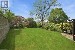 Expansive backyard featuring a large lawn, established landscaping, a wooden perimeter fence, and a dark-toned outdoor pergola - 