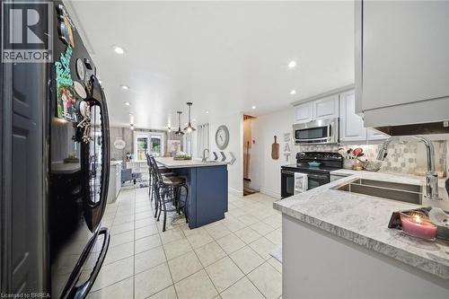Bright kitchen featuring a central island with seating, pendant lighting, stainless steel appliances, light cabinetry, and tiled flooring - 62 East Avenue, Brantford, ON 