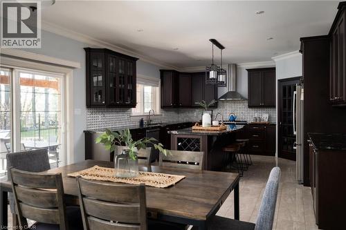 Spacious kitchen featuring dark wood cabinetry, dark countertops, a tiled backsplash, stainless steel appliances, and a central island with integrated wine storage - 1505 Milburough Line, Carlisle, ON 
