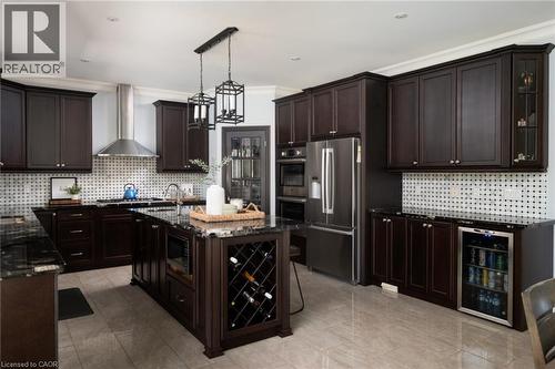 Kitchen featuring dark wood cabinetry, stainless steel appliances, a center island with wine storage, granite countertops, and tile flooring - 1505 Milburough Line, Carlisle, ON 