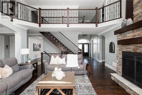 Two-story living area featuring a stone fireplace with a wood mantle, a grand staircase with wrought iron balusters, a second-story open walkway, and dark wood-finish flooring - 1505 Milburough Line, Carlisle, ON 