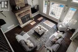Stone-clad fireplace with wood mantle, dark wood-finish flooring, tall windows, and recessed lighting - 