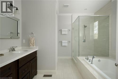 Spacious bathroom featuring a dark wood-finish vanity with a light-toned countertop, a frameless glass-enclosed shower, a built-in soaking tub, and light-toned tile flooring - 1505 Milburough Line, Carlisle, ON 