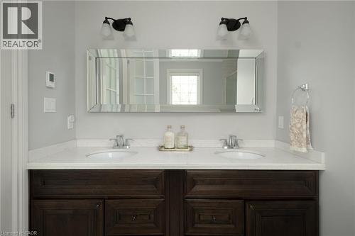 Dual vanities with undermount sinks, white solid-surface countertop, dark wood-finish cabinetry, and a beveled mirror - 1505 Milburough Line, Carlisle, ON 