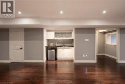 Dark wood-finish flooring, recessed lighting, and a wet bar featuring white cabinetry, a dark countertop, and a tiled backsplash - 