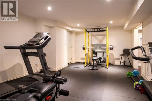 Recessed lighting illuminates the space, featuring a full-height yellow power rack, rubber floor tiles, and a white paneled door - 1505 Milburough Line, Carlisle, ON 