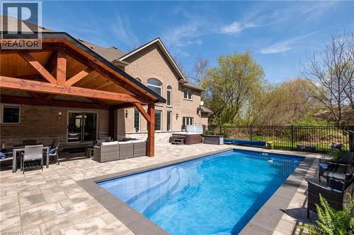 Expansive paver patio with an in-ground swimming pool, hot tub, and a covered outdoor living area featuring a wood-beam roof structure - 1505 Milburough Line, Carlisle, ON 