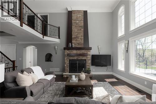 Two-story living area featuring a stone fireplace, wood-finish flooring, and a second-story balcony with wrought iron railing - 1505 Milburough Line, Carlisle, ON 