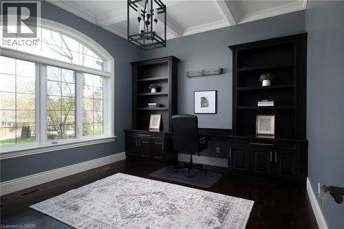 Arched window, dark wood-finish flooring, coffered ceiling, built-in shelving, and a modern chandelier - 1505 Milburough Line, Carlisle, ON 