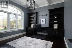 Arched window, dark wood-finish flooring, coffered ceiling, built-in shelving, and a modern chandelier - 