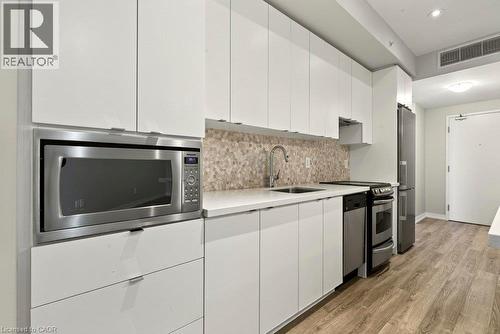 Contemporary kitchen featuring white flat-panel cabinetry, stainless steel appliances, a mosaic tile backsplash, light-toned countertops, and wood-finish flooring - 457 Plains Road Unit# 225, Burlington, ON 