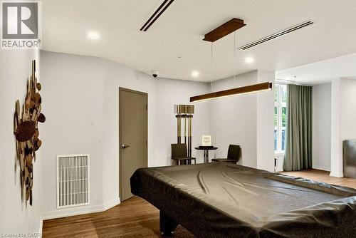 Spacious recreation area featuring wood-finish flooring, a contemporary linear pendant light, recessed lighting, and a large window with floor-length drapes - 457 Plains Road Unit# 225, Burlington, ON 