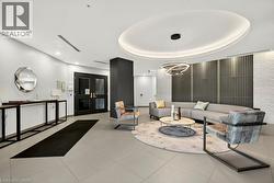 Modern lobby featuring light-toned tile flooring, a circular ceiling detail with recessed lighting, a contemporary chandelier, textured wall panels, and double entry doors - 