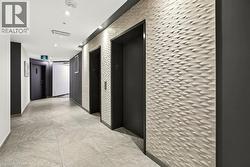 Hallway featuring two elevators with dark doors, a textured geometric accent wall, recessed lighting, and large format floor tiling - 