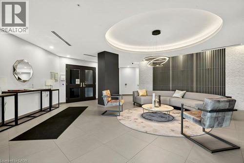 Modern lobby featuring light-toned tile flooring, a circular ceiling detail with recessed lighting, a contemporary chandelier, textured wall panels, and double entry doors - 457 Plains Road Unit# 225, Burlington, ON 