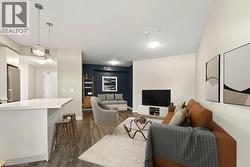 Open-concept living space featuring wood-finish flooring, a kitchen island with a white countertop, two pendant lights, and recessed ceiling lighting - 
