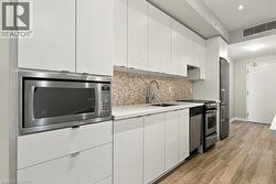 Contemporary kitchen featuring white flat-panel cabinetry, stainless steel appliances, a mosaic tile backsplash, light-toned countertops, and wood-finish flooring - 