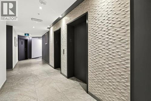 Hallway featuring two elevators with dark doors, a textured geometric accent wall, recessed lighting, and large format floor tiling - 457 Plains Road Unit# 225, Burlington, ON 