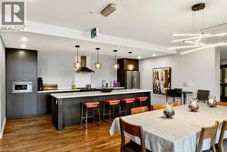 Open-concept kitchen and dining area featuring rich wood-finish flooring, dark wood-finish cabinetry, a large kitchen island with white countertop, and a modern linear chandelier - 
