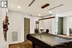Spacious recreation area featuring wood-finish flooring, a contemporary linear pendant light, recessed lighting, and a large window with floor-length drapes - 