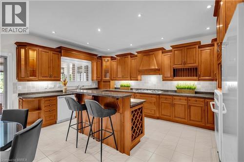 Spacious kitchen featuring extensive wood cabinetry, granite countertops, tile flooring, a central island with integrated wine storage, and a built-in range hood - 302 German School Road, Paris, ON 