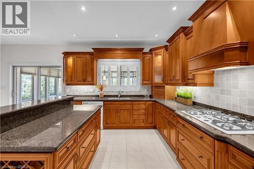 Kitchen featuring extensive wood cabinetry, granite countertops, tile flooring, and a built-in gas range - 302 German School Road, Paris, ON 