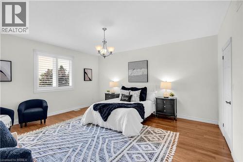Room featuring wood-finish flooring, a contemporary chandelier, white walls, and a window with white plantation shutters - 302 German School Road, Paris, ON 