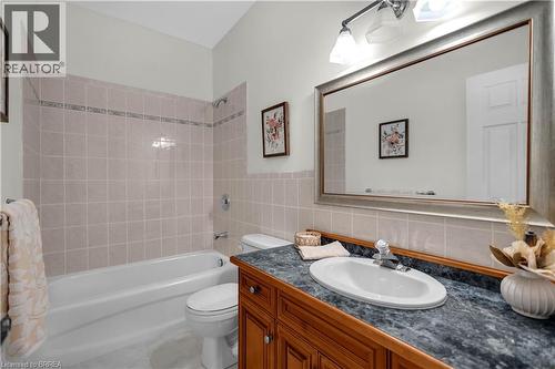 Bathroom featuring a white bathtub with light-toned tiled surround, a toilet, and a vanity with a dark speckled countertop, an oval undermount sink, and a framed mirror under a three-light fixture - 302 German School Road, Paris, ON 