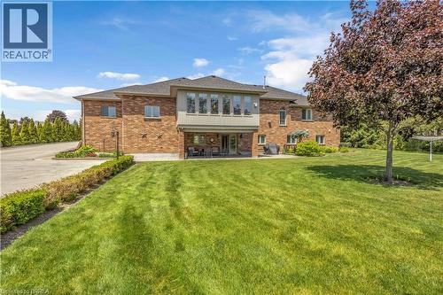 Rear exterior featuring brick construction with a second-story bay window, ground-level patio, and extensive lawn area - 302 German School Road, Paris, ON 