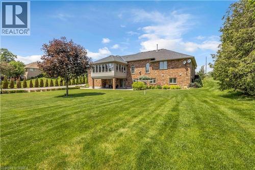 Expansive rear lawn featuring a mature tree and landscaped beds - 302 German School Road, Paris, ON 