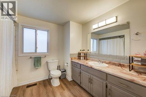 Bathroom featuring a single window, a large vanity with a single sink, a toilet, wood-finish flooring, and a subway tile backsplash - 143 Sunrise Place, Kitchener, ON 