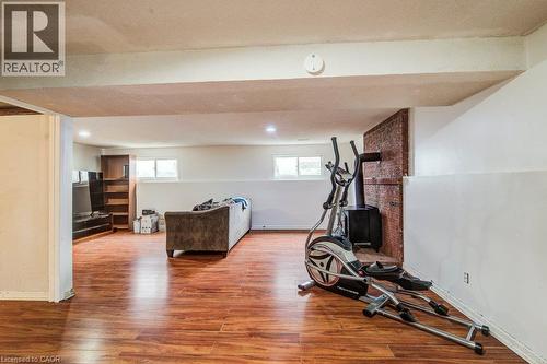 Expansive finished basement with wood-finish flooring, recessed lighting, and a brick-clad fireplace feature - 143 Sunrise Place, Kitchener, ON 