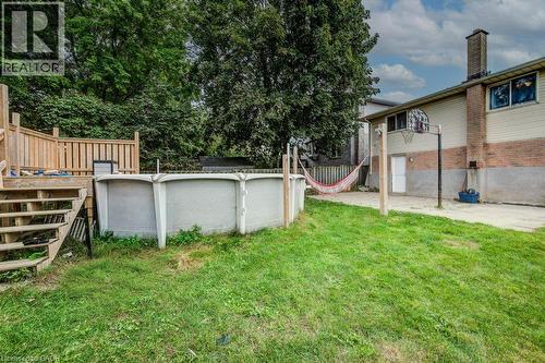 Expansive backyard featuring a wood deck with stairs and railing, an above-ground pool, a concrete patio area, and a basketball hoop - 143 Sunrise Place, Kitchener, ON 