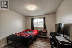 Bright secondary bedroom featuring wood-finish flooring, recessed ceiling lighting, and a large window with blackout curtains - 