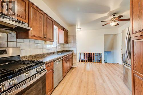 Wood-finish flooring, stainless steel appliances, wood cabinetry, tile backsplash, and a ceiling fan - 143 Sunrise Place, Kitchener, ON 