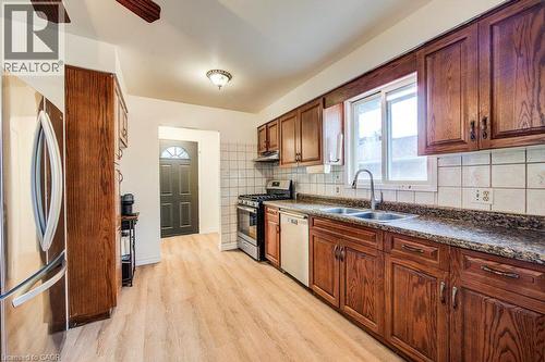 Galley kitchen showcasing wood-finish cabinetry with hardware accents, stainless steel appliances including a refrigerator and range, granite-style countertops, subway tile backsplash, and wood-finish - 143 Sunrise Place, Kitchener, ON 